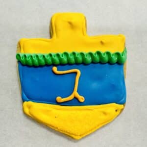 Royal iced dreidel cookie. Yellow top and bottom, a rippled green band at the top, and a blue band in the middle. In yellow frosting is the Hebrew letter "gimel".