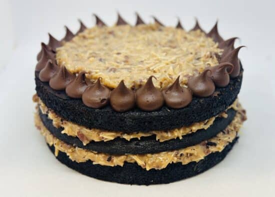 Three layers of chocolate cake with layers of coconut filling. Cake topped with coconut filling inside a ring of piped chocolate ganache.